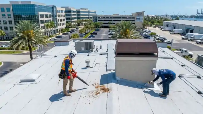 Commercial roofing crew cleaning debris with a blower and resealing flashing around a roof penetration on a flat commercial roof in Clearwater FL.
